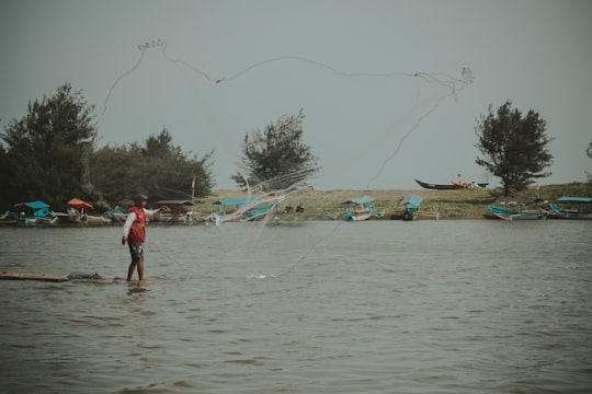 man in red t-shirt and black shorts standing on water during daytime in Kulon Progo Indonesia