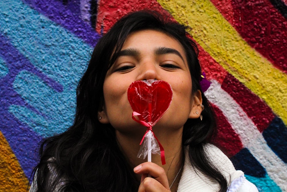 woman in white long sleeve shirt holding red lollipop