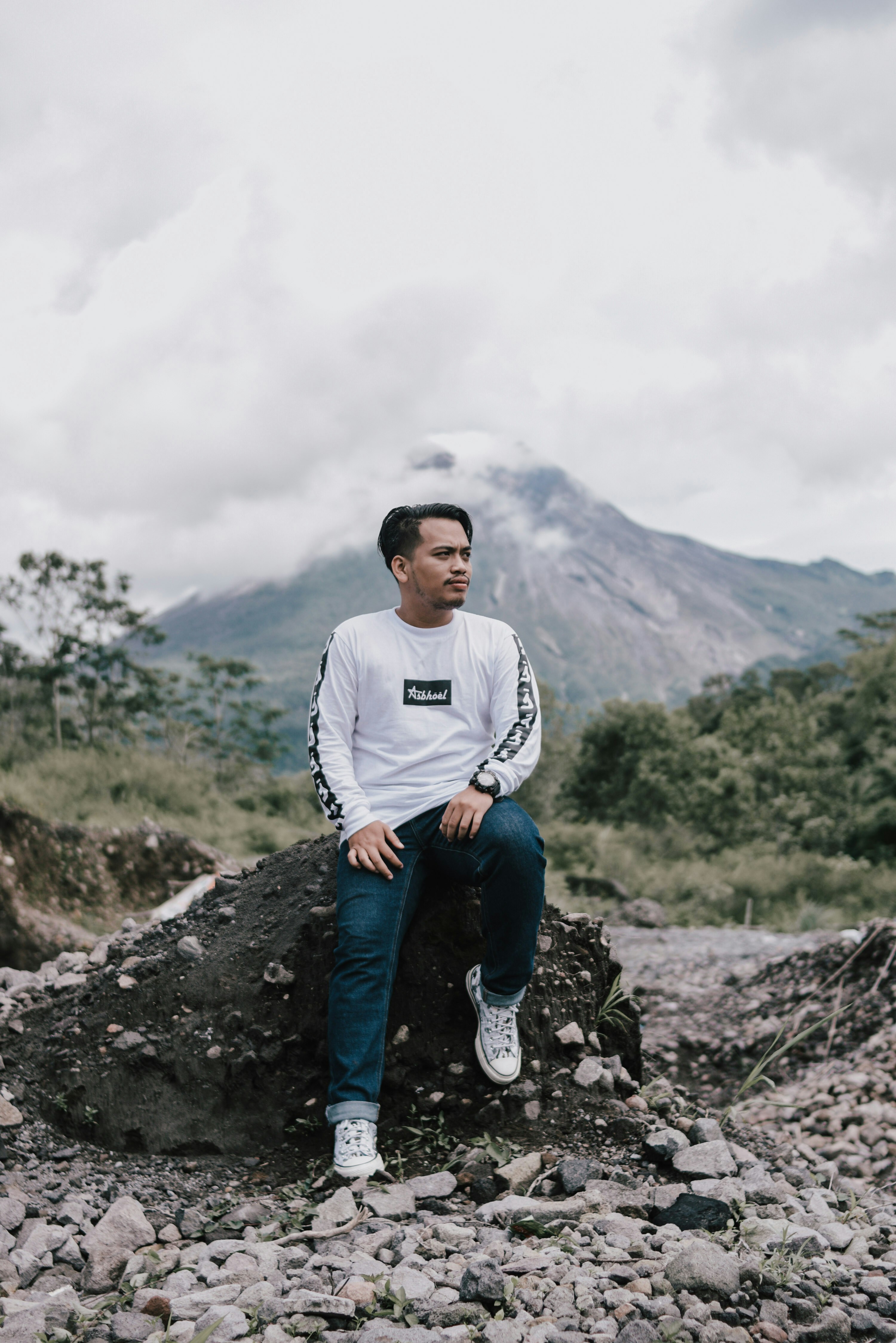 man in white crew neck t-shirt and blue denim jeans sitting on rock during daytime