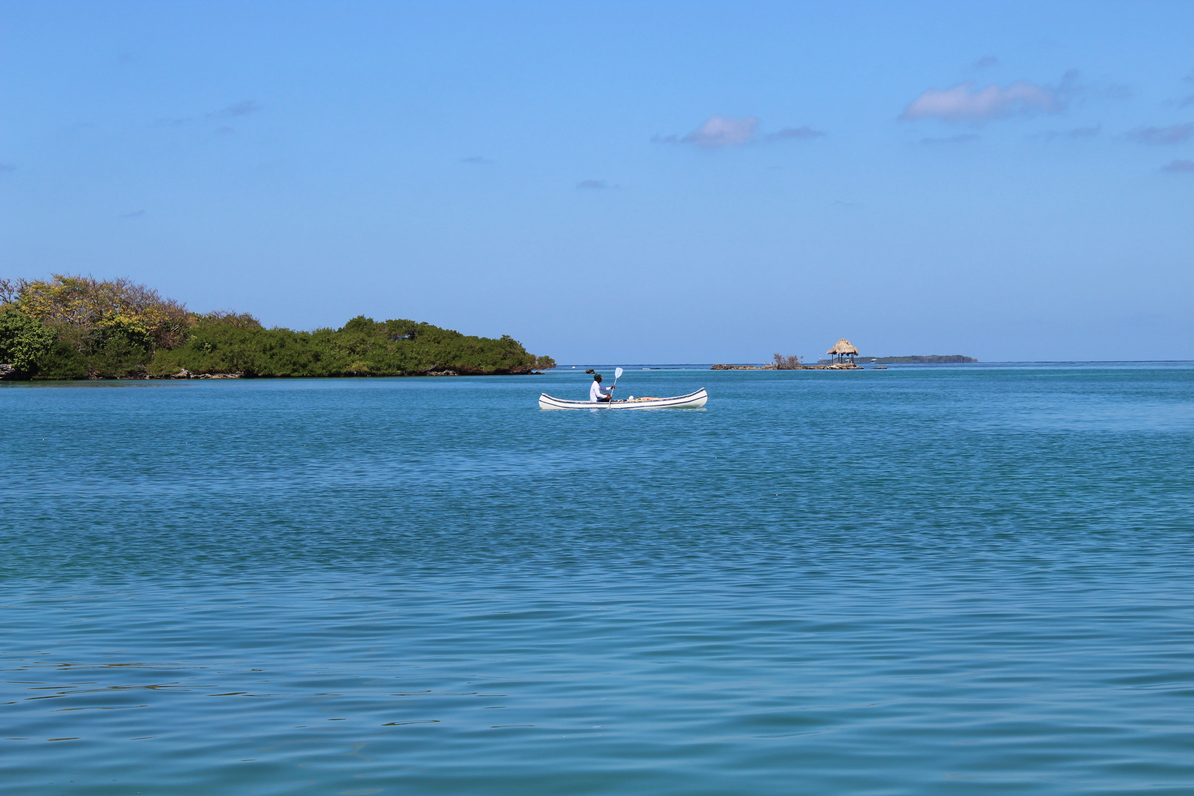 A person paddles a canoe across calm turquoise water near a mangrove island outside Cartagena.