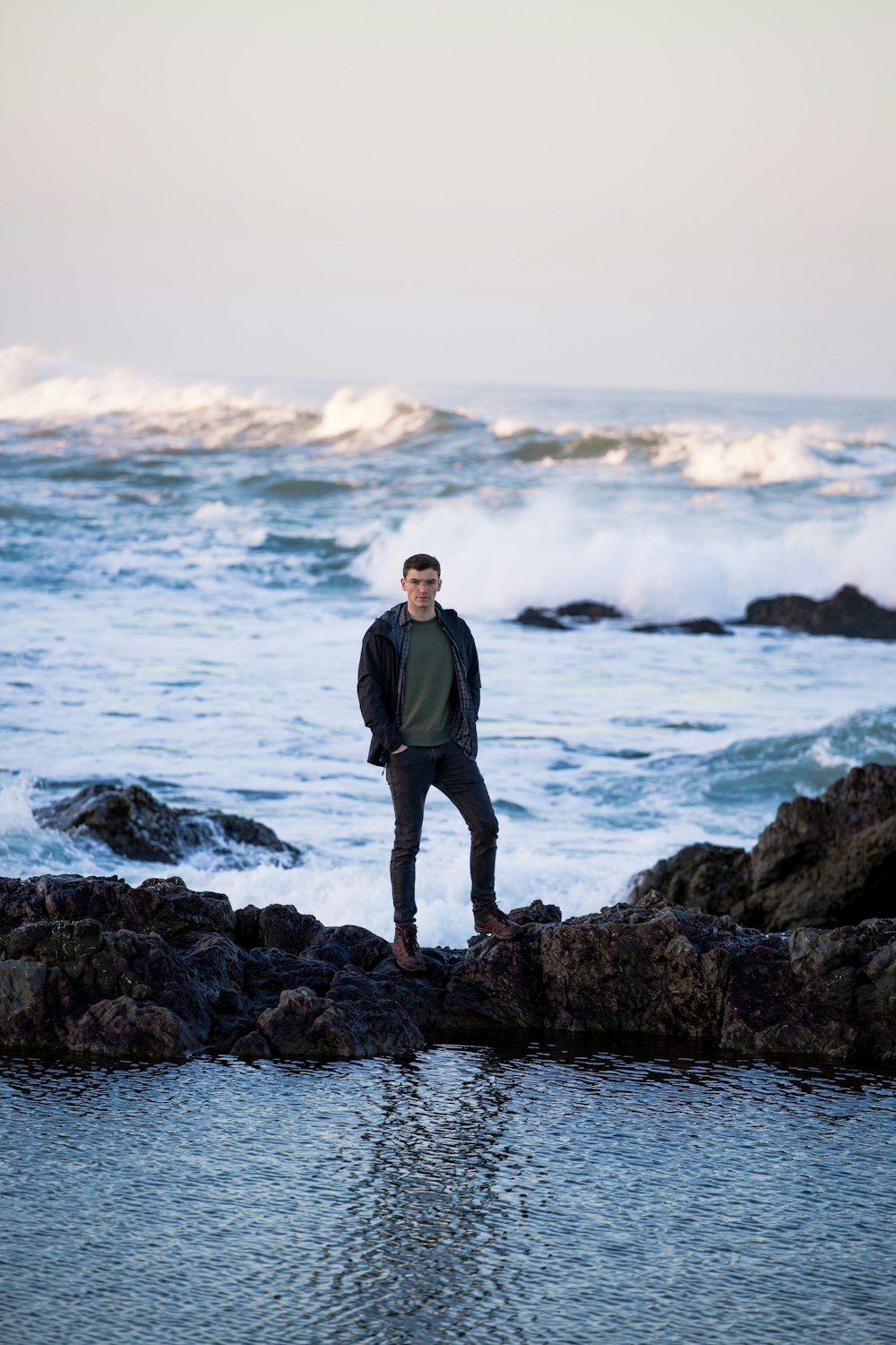 man in black jacket standing on rock near sea during daytime