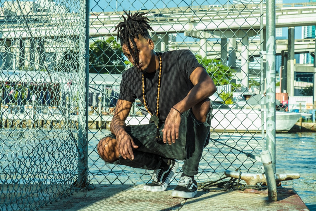 man in black crew neck t-shirt and blue denim jeans sitting on gray metal fence