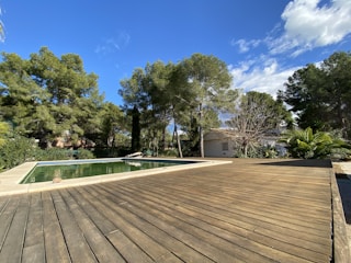 A beautifully crafted wooden deck beside a sparkling pool under the afternoon sun.