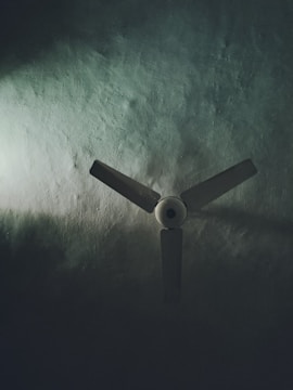 A three-blade ceiling fan set against a textured surface, partially illuminated by soft light emphasizing shadows