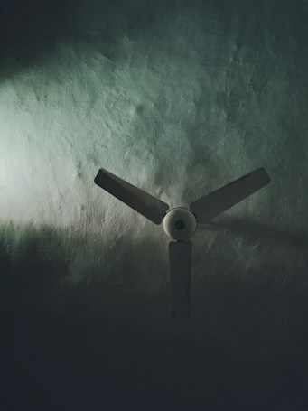 A three-blade ceiling fan set against a textured surface, partially illuminated by soft light emphasizing shadows