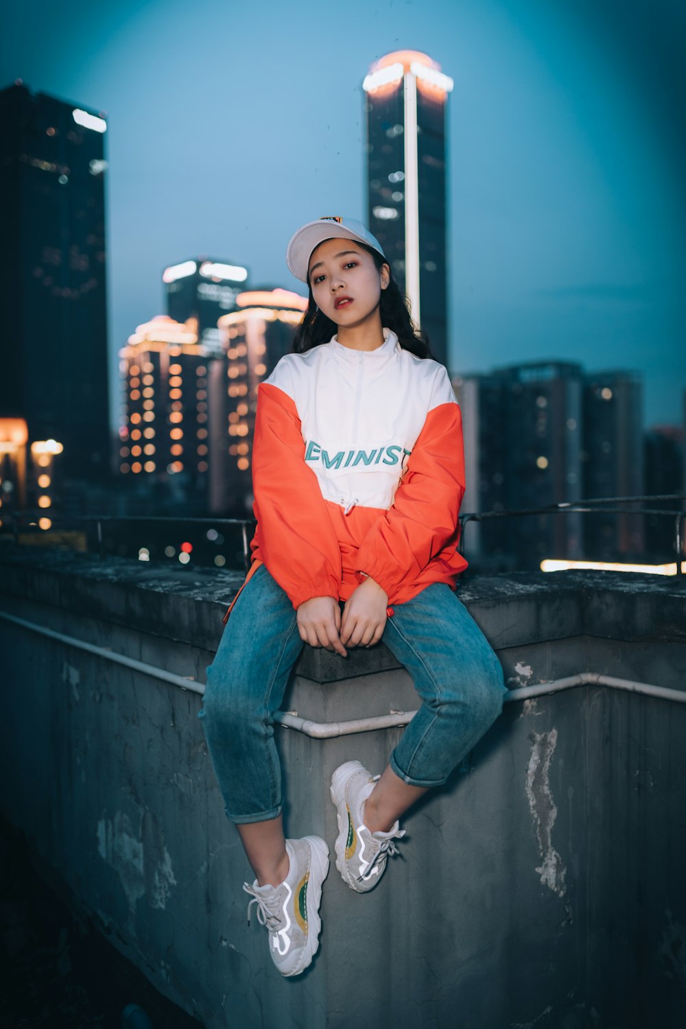 Mujer con camisa de manga larga roja y blanca y jeans de mezclilla azules sentada sobre concreto gris