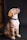 A young Labrador puppy with a light brown fur coat, sitting upright and gazing upward. It wears a blue collar with a pattern of white bones against a contrasting dark background.