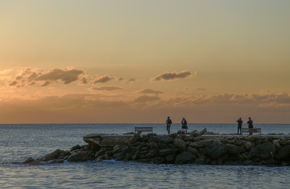 people standing on rocky shore during sunset
