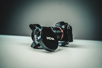 A professional camera with a lens attached is positioned on a flat surface. The background is softly blurred, creating a focus on the sleek design of the camera, which features a Sony logo and a Laowa lens cap.