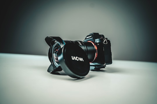 A professional camera with a lens attached is positioned on a flat surface. The background is softly blurred, creating a focus on the sleek design of the camera, which features a Sony logo and a Laowa lens cap.