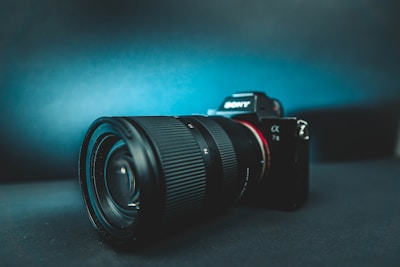 A high-quality camera with a large lens, prominently displaying the Sony logo. It rests on a dark surface, with a gradient background transitioning from dark to light blue, enhancing the sleek and professional appearance of the camera.