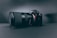 A professional camera with a large zoom lens is positioned at a slight angle, set against a smooth, dark, matte background. The camera and lens are prominently displayed, with the brand name visible on the camera body.