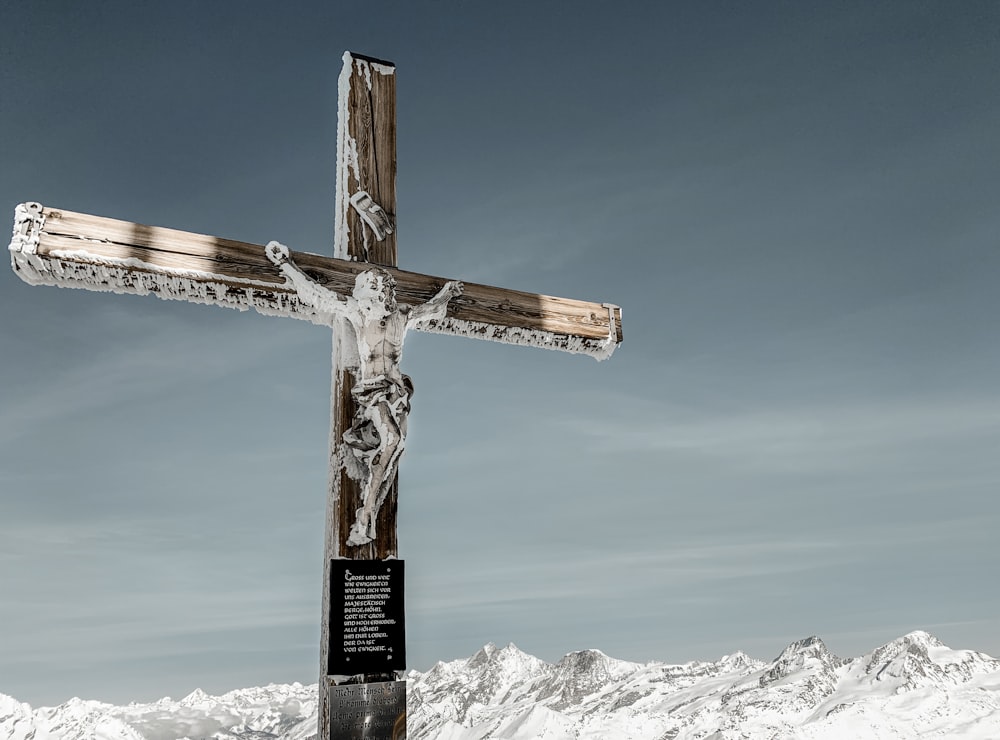 昼間の青空の下で雪に覆われた山に茶色の木製の十字架