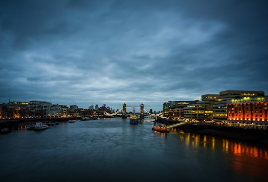 body of water near city buildings under cloudy sky during daytime in Tower Bridge United Kingdom
