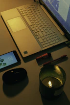 A warm, inviting desk setup with a lit candle, a notebook, and a smartphone displaying a WhatsApp chat.