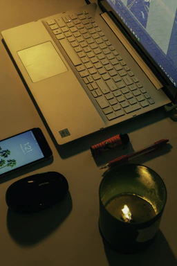A warm, inviting desk with a notebook, pen, and a softly glowing candle beside a laptop.