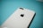 A close-up of a white smartphone with a prominent Apple logo, placed on a turquoise surface. The camera and flash are visible on the top corner of the phone.