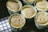 Several light brown, fluffy pastries are sitting in decorative paper cups resting on a black cooling rack. The pastries have a soft, slightly wrinkled surface, suggesting they are freshly baked and possibly cheesecakes or sponge cakes.