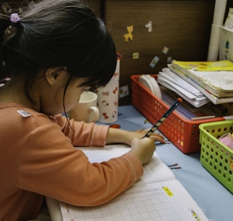 girl in pink long sleeve shirt writing on white paper