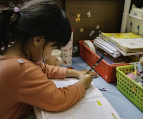 girl in pink long sleeve shirt writing on white paper