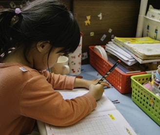 girl in pink long sleeve shirt writing on white paper