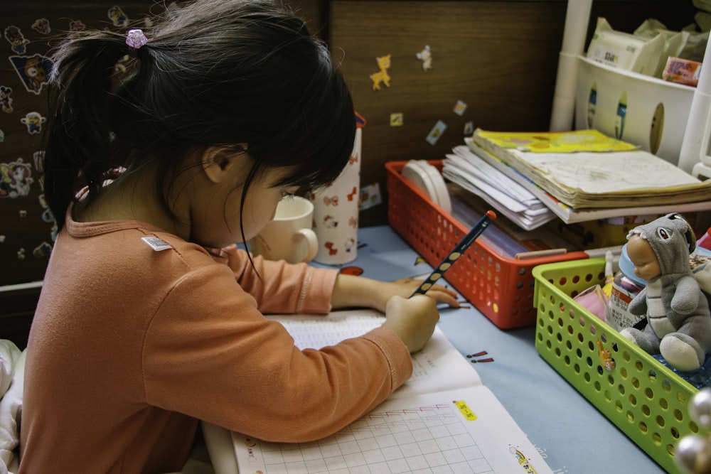 menina na camisa rosa de manga comprida que escreve no papel branco