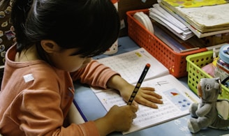 girl in orange long sleeve shirt writing on white paper