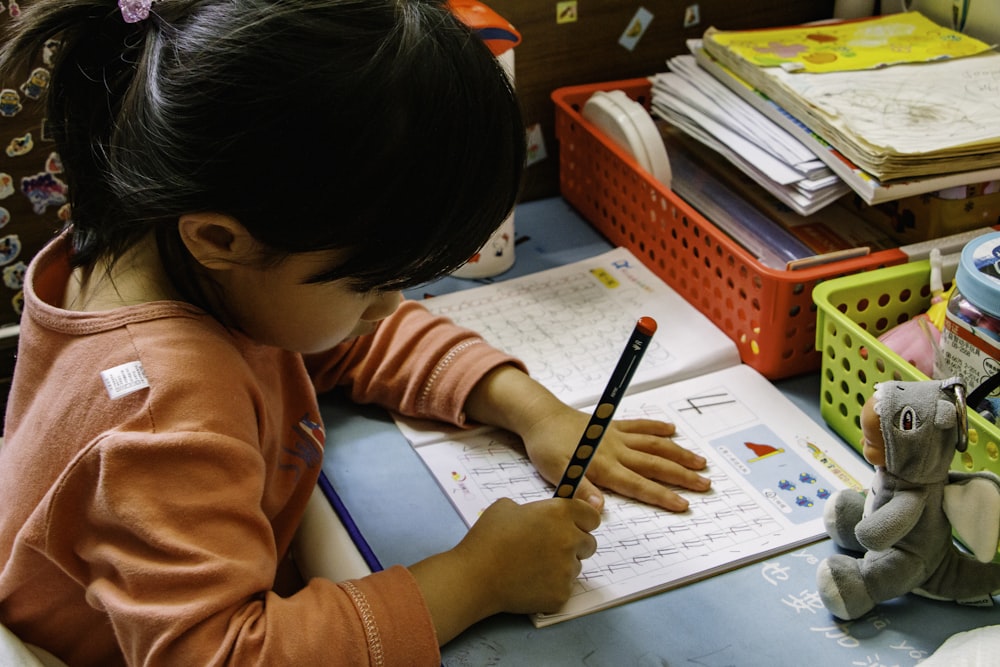 girl in orange long sleeve shirt writing on white paper