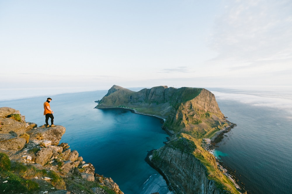 man in black shirt and black pants standing on rock formation near blue sea during daytime