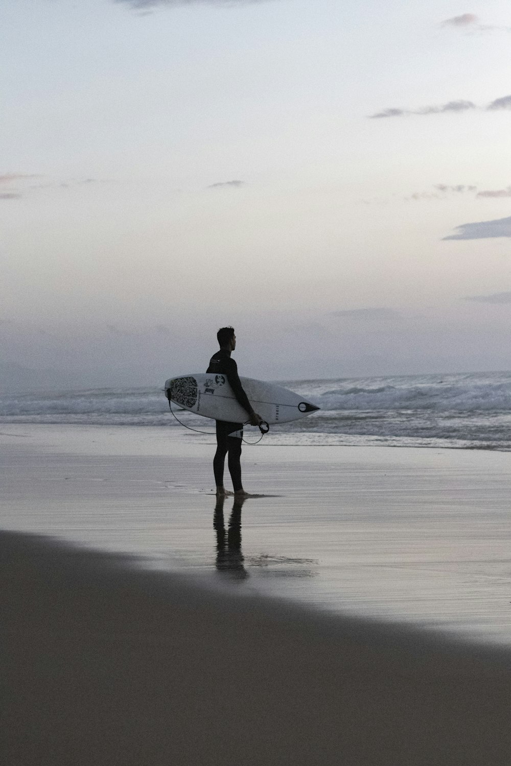 Mann im weißen Hemd mit weißem Surfbrett, der tagsüber am Strand spazieren geht