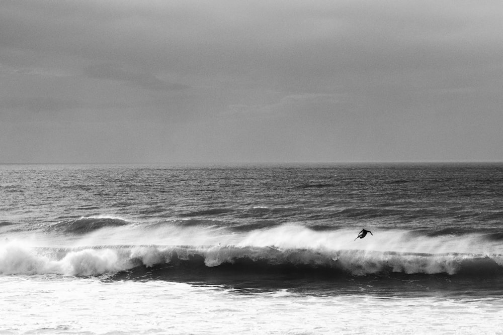 grayscale photo of person surfing on sea waves