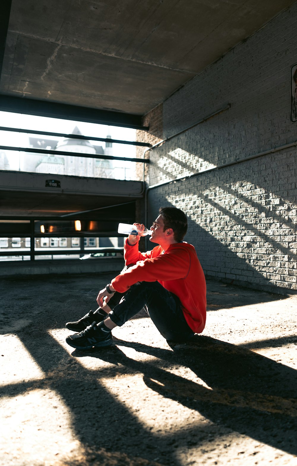 man in red jacket and black pants sitting on brown wooden bench