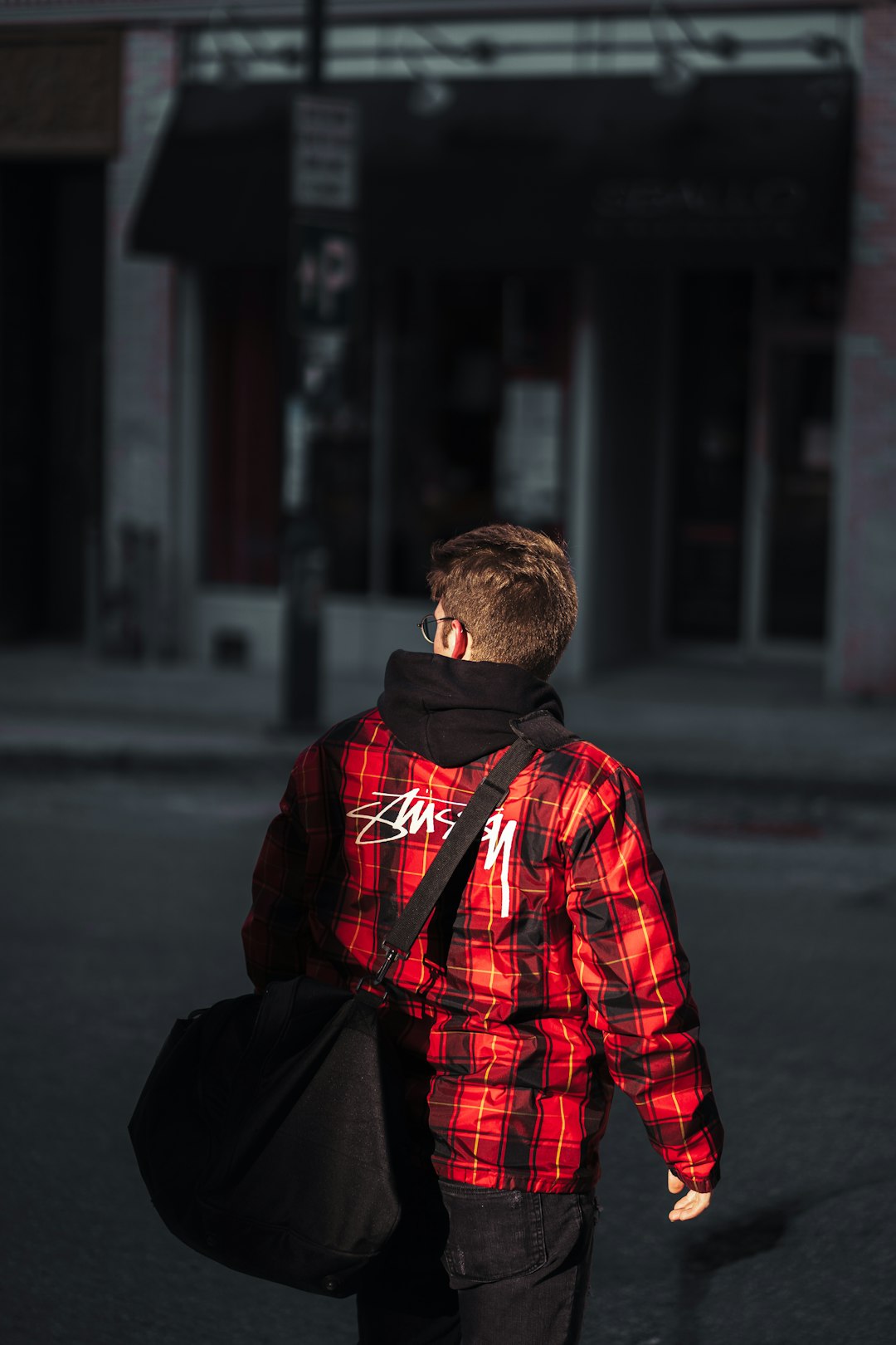 man in red and black plaid dress shirt and black pants sitting on sidewalk during daytime