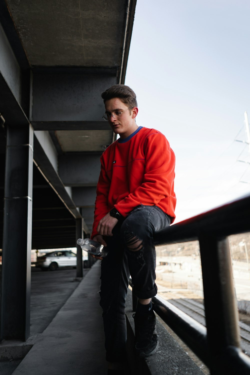 man in red sweater and black pants sitting on gray concrete wall during daytime
