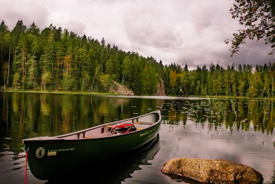 red and white canoe on lake near green trees under white clouds during daytime Finland