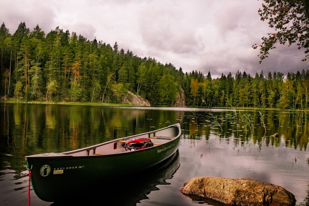canoa vermelha e branca no lago perto de árvores verdes sob nuvens brancas durante o dia
