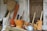 A collection of traditional wooden kitchen utensils and tools is arranged in front of a rustic wooden door. The assortment includes wooden mortars, pestles, a silver kettle, and a large woven basket. The background features textured, weathered walls adding to the rustic charm.