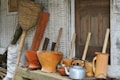 A collection of traditional wooden kitchen utensils and tools is arranged in front of a rustic wooden door. The assortment includes wooden mortars, pestles, a silver kettle, and a large woven basket. The background features textured, weathered walls adding to the rustic charm.