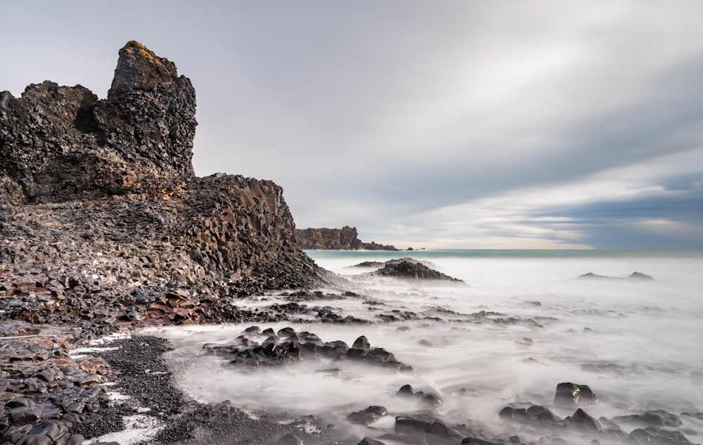 brown rock formation on sea under white clouds during daytime