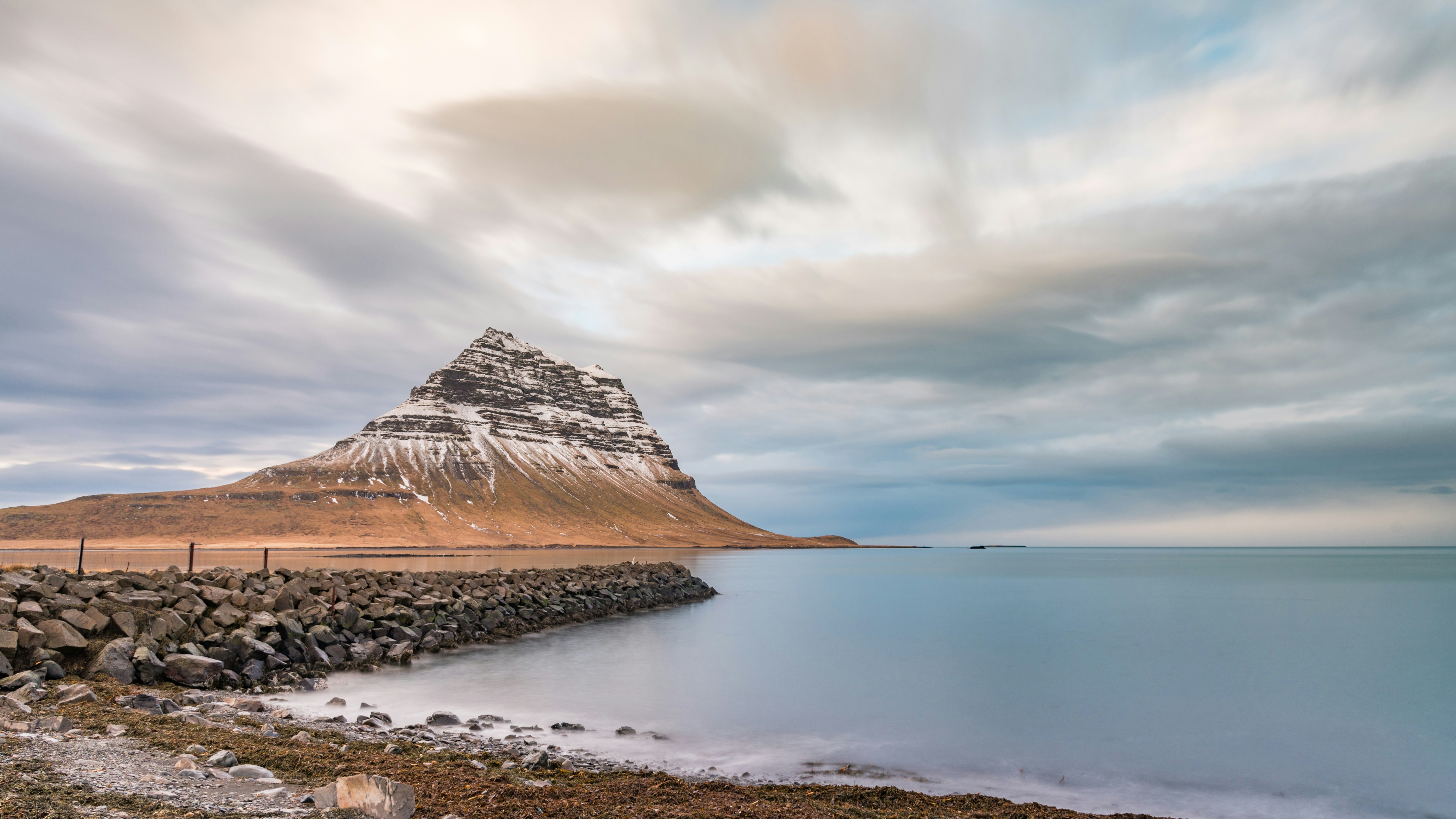 brown mountain near body of water under cloudy sky during daytime