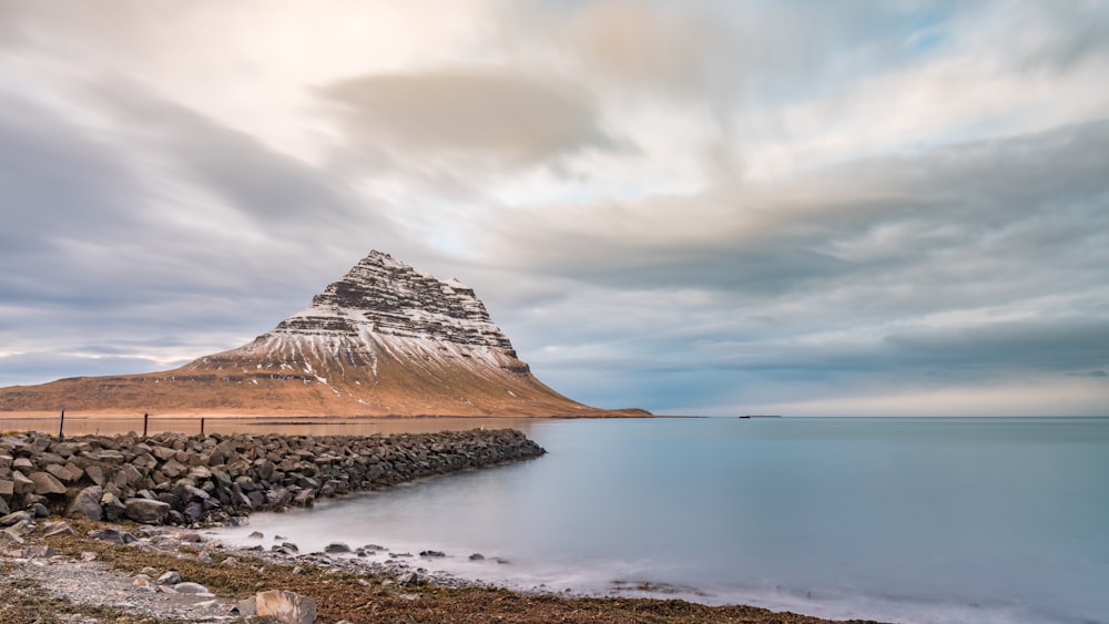 brown mountain near body of water under cloudy sky during daytime