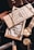 An arrangement of men's accessories including a wooden box labeled 'Bourbon Cedar' with a chain draped over it. Surrounding items include a gold wristwatch, a leather wallet, sunglasses, and a knife with a wooden handle. The composition suggests a theme of luxury and sophistication.