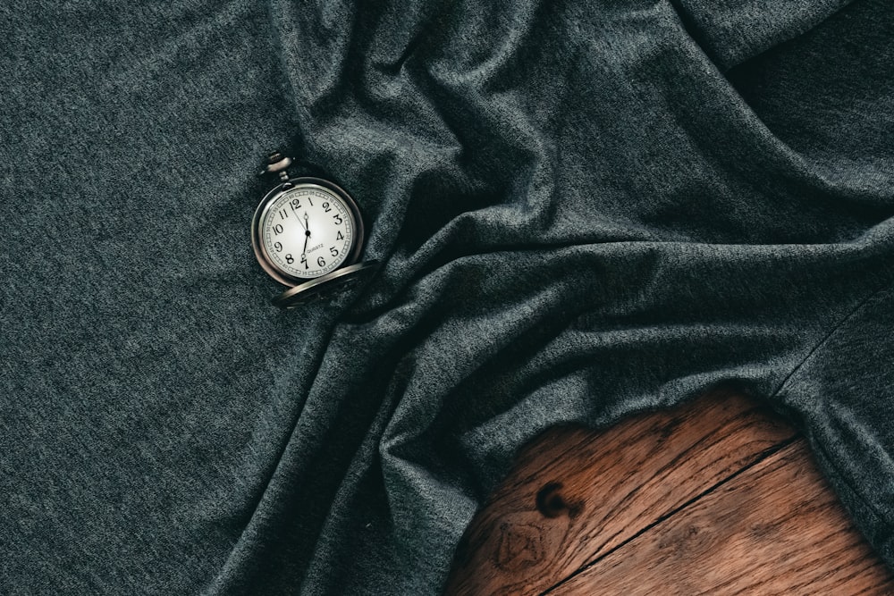 Reloj de bolsillo plateado y blanco sobre textil negro