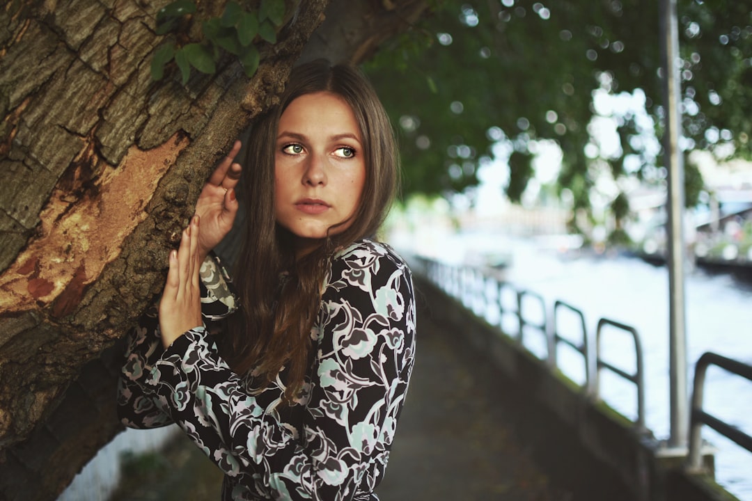 woman in black and white floral long sleeve shirt standing beside brown tree