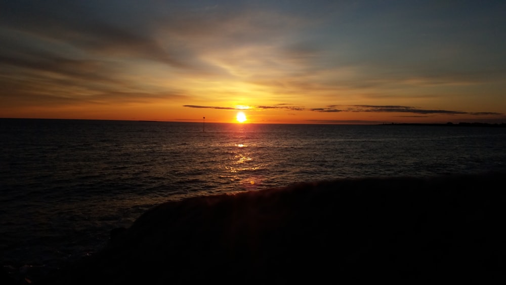 silhouette of person standing on seashore during sunset