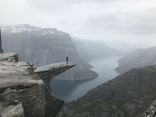 person standing on rock formation near river during daytime in Trolltunga Norway