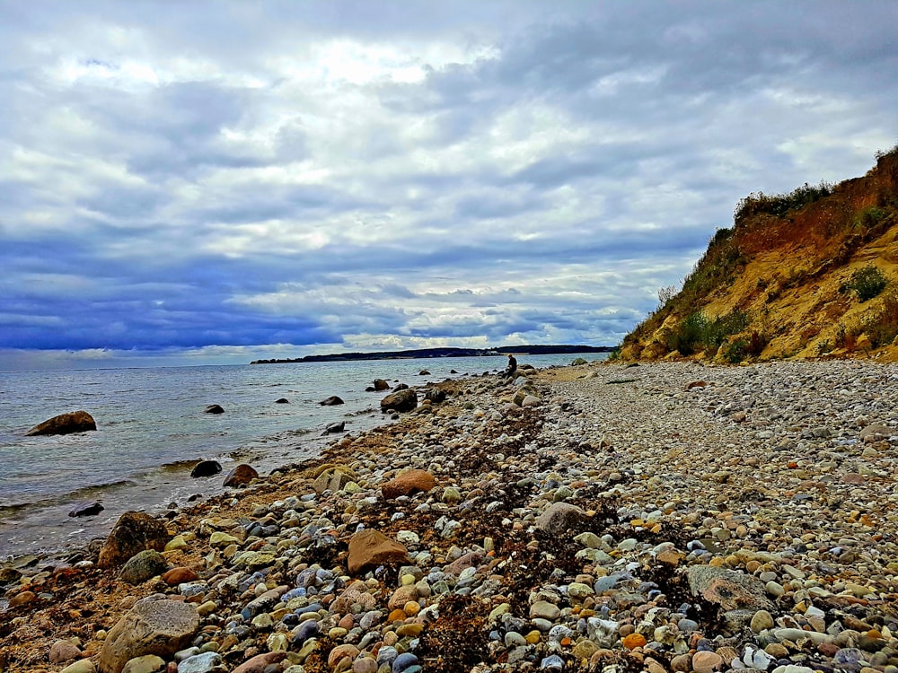 brown rocks on seashore under white clouds and blue sky during daytime