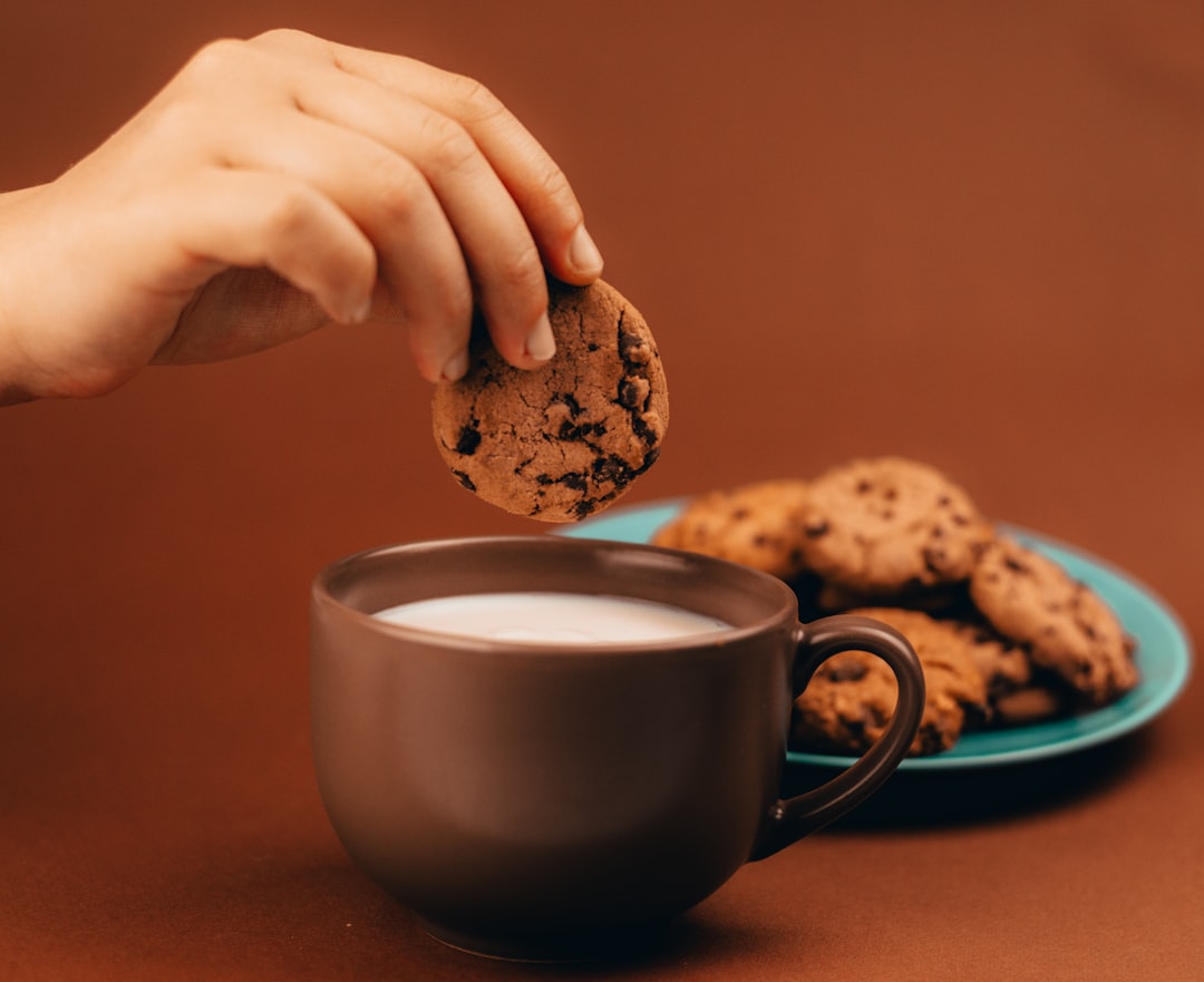 person holding white ceramic mug with coffee, Milk and cookies on brown background