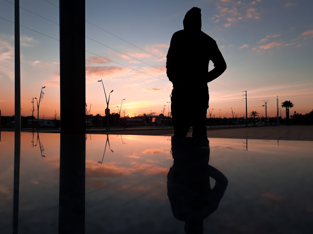 silhouette of man standing near body of water during sunset