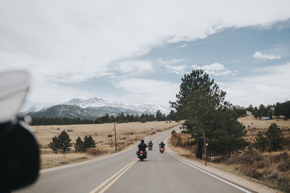 moto noire sur la route près des arbres verts et de la montagne pendant la journée